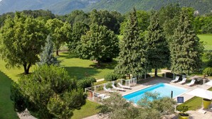 Un espace piscine doté de chaises longues, entouré d’arbres et offrant une vue sur un paysage montagneux.