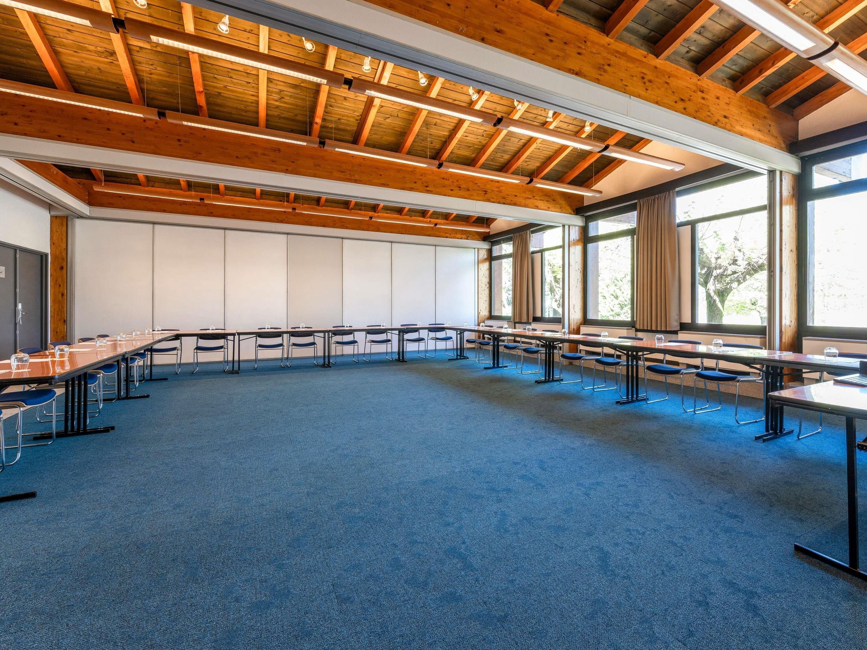 Un salón de conferencias con una larga mesa, sillas y ventanas grandes.