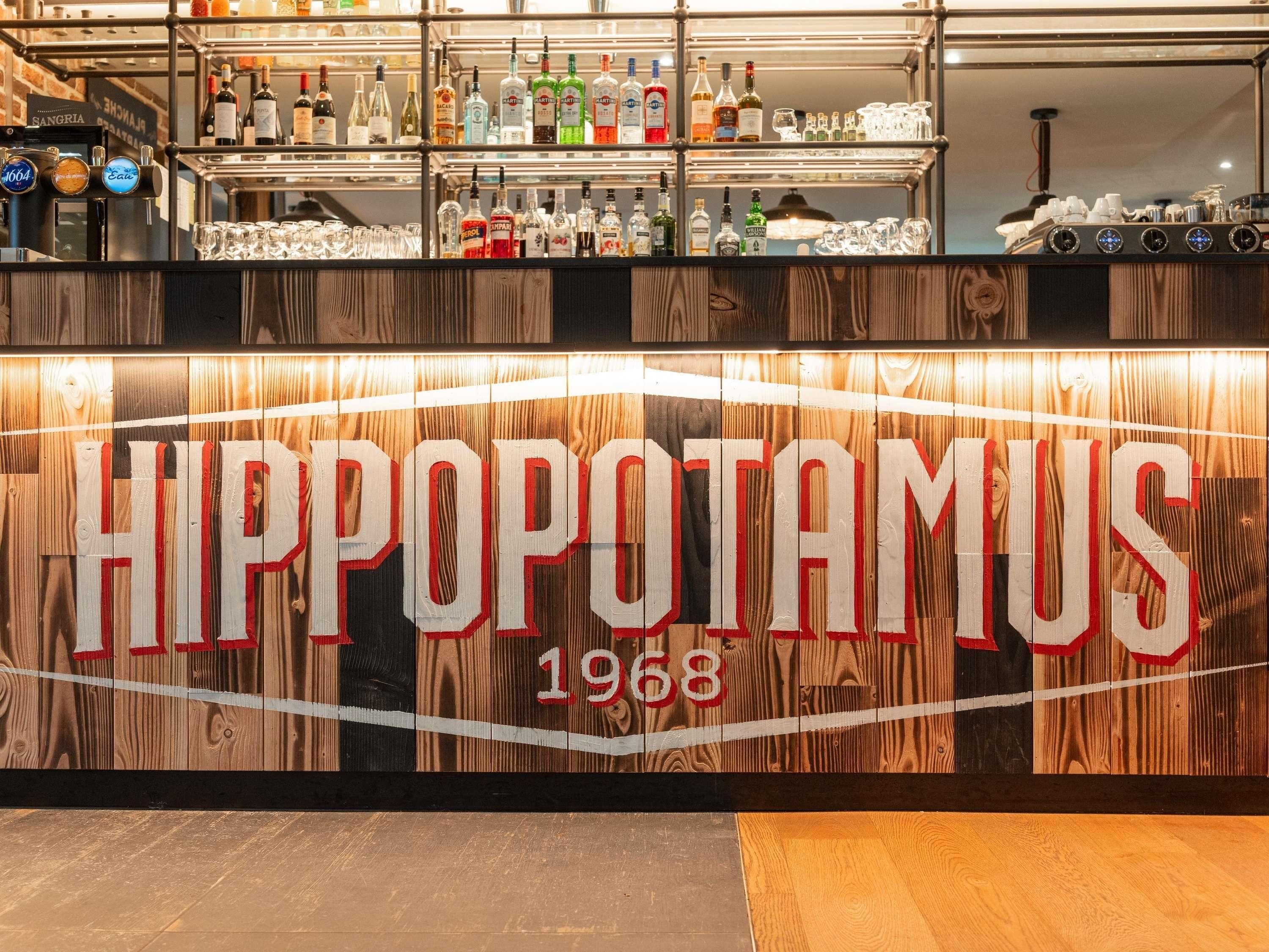 A bar area with a wooden sign reading 'HIPPOPOTAMUS 1968' and shelves of liquor bottles.