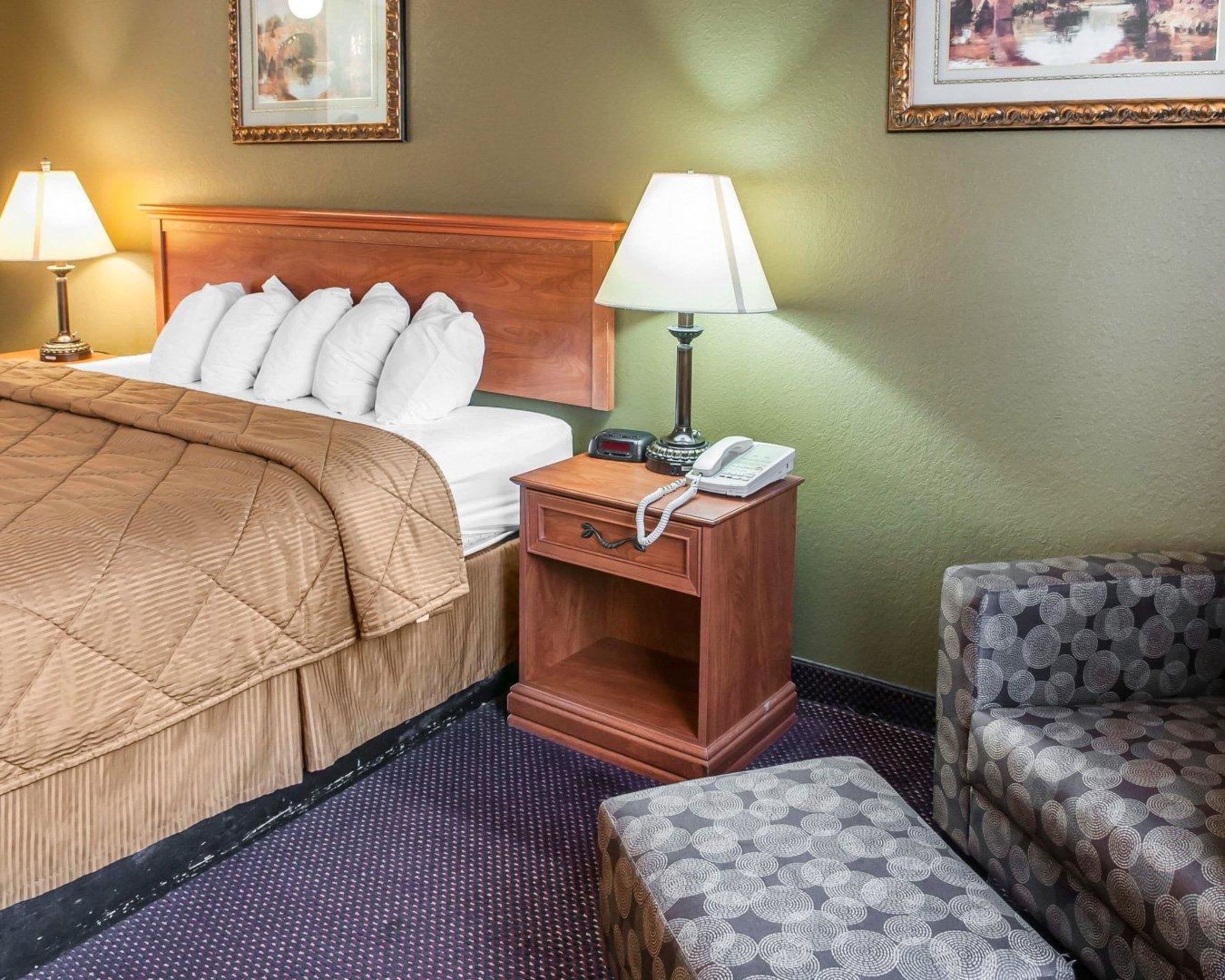 Een hotelkamer met een bed, een nachtkastje met een telefoon, een stoel en een vloerbedekking.
