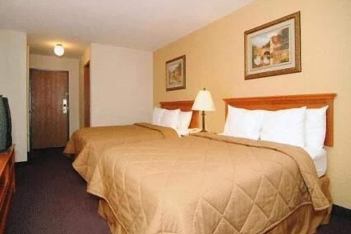 A hotel room with two beds, a wooden headboard, a bedside lamp, and a framed picture on the wall.
