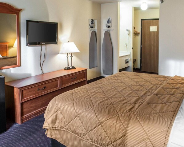 Una habitación de hotel con cama, televisión, tabla de planchar y espejo.