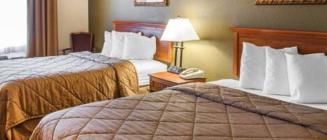 A hotel room with two queen beds, a bedside table with a lamp, a phone, and two framed pictures on the wall.
