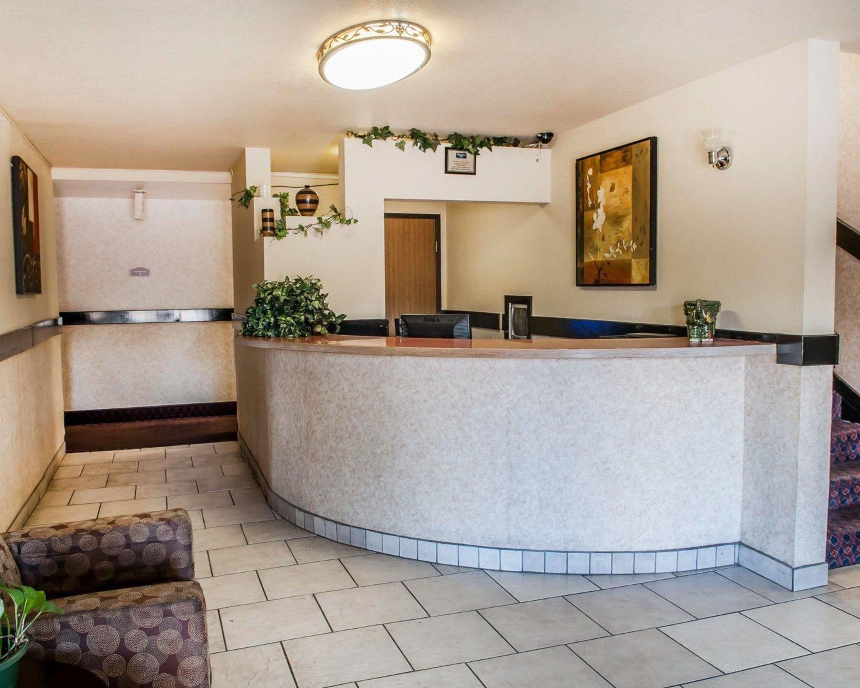 A reception area with a curved reception desk, a potted plant, a framed artwork, and a staircase to the right.