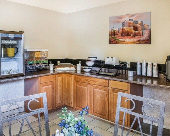 A kitchen with a granite countertop, wooden cabinets, a coffee station, and a painting on the wall.