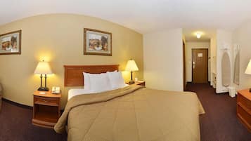 Una habitación de hotel con una cama grande, dos lámparas de noche, un cabecero de madera, una mesita de noche y una puerta que da a un pasillo con un espejo y un perchero.