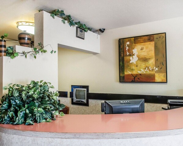 A reception area with a large potted plant, a framed artwork on the wall, and a flat-screen TV mounted above a desk.