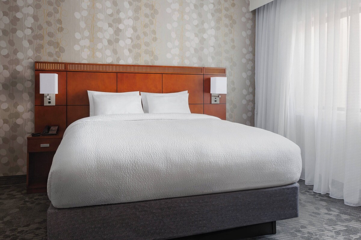 A large bed with a wooden headboard, two bedside lamps, and a nightstand with a phone.