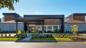 Um hotel Courtyard by Marriott com design moderno, apresentando uma entrada coberta e jardins bem cuidados.