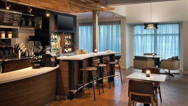 Uma área de bar moderna com balcão de madeira, banquetas e uma tela de televisão.