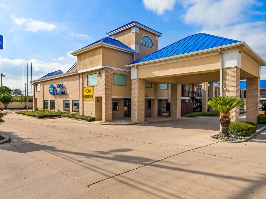A Best Western hotel with a blue roof, a 'NOW HIRING' sign, and a clear sky.