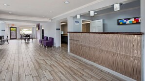 Un'hall dell'hotel con pavimento in legno a spina di pesce, sedute viola e una reception con uno sfondo decorato.