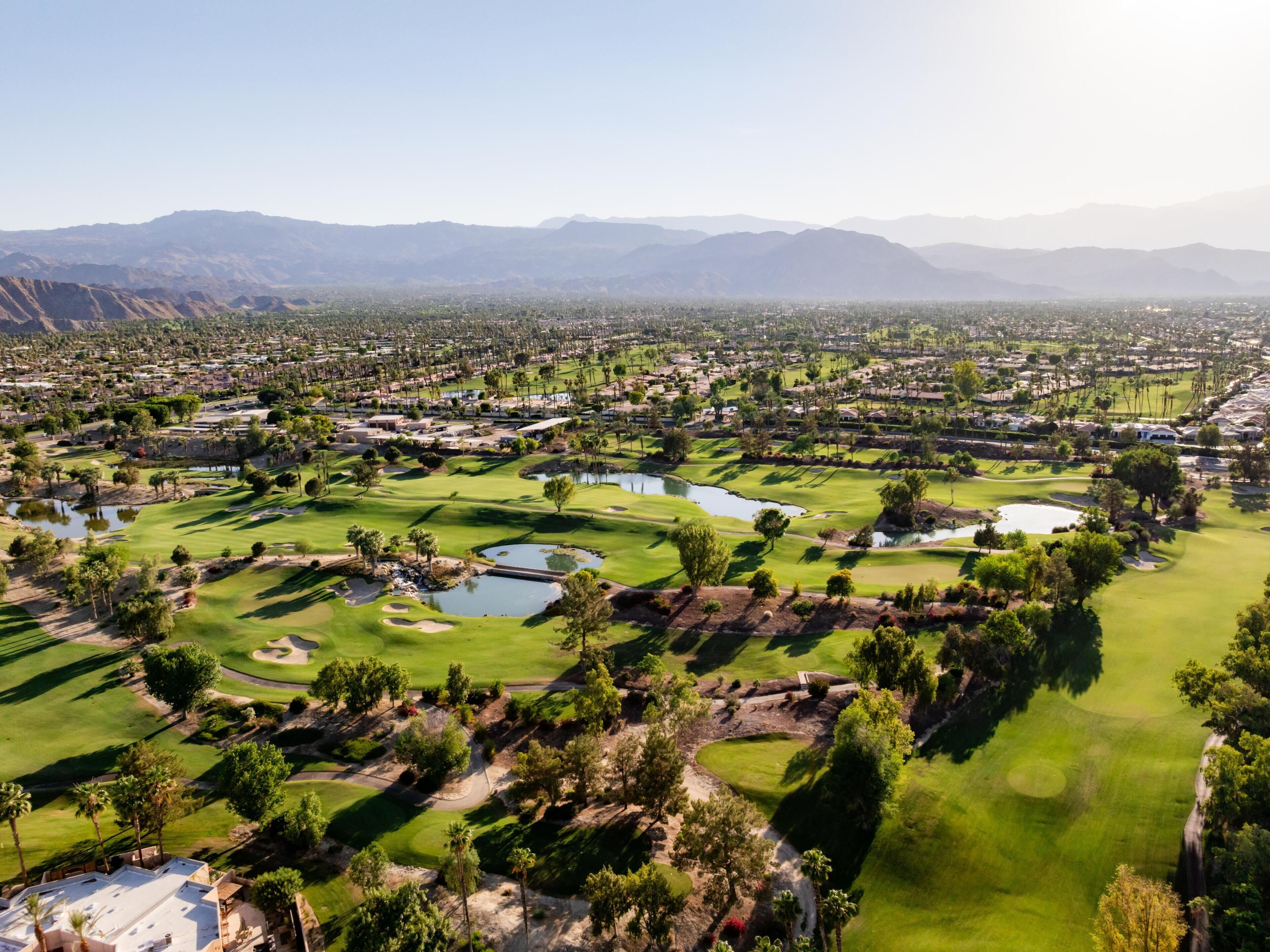 A golf course with multiple ponds, surrounded by residential areas and mountains in the background.