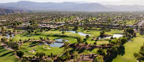 A golf course with multiple ponds, surrounded by residential areas and mountains in the background.