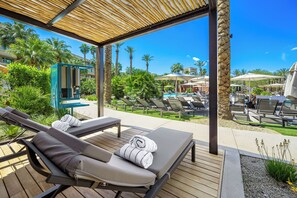 A covered outdoor lounge area with sun loungers, a pool, and palm trees. - Grand Hyatt Indian Wells Resort & Villas (Indian Wells)