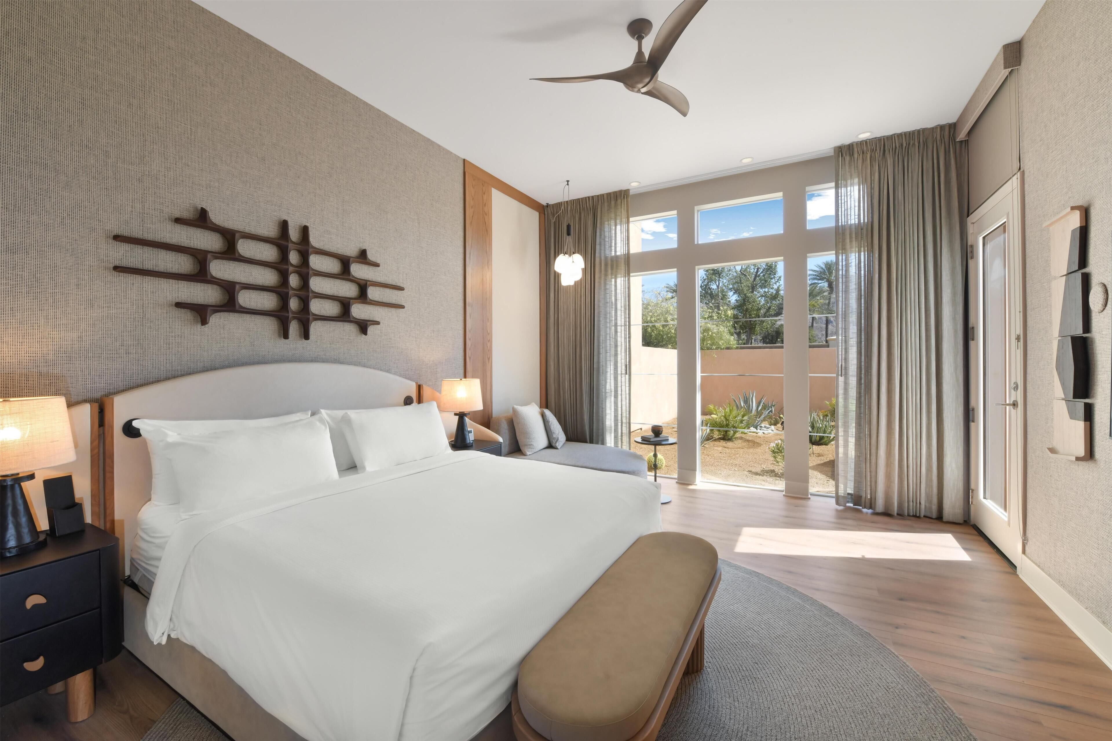 A hotel room with a large bed, a ceiling fan, a TV, and a view of the outdoors.