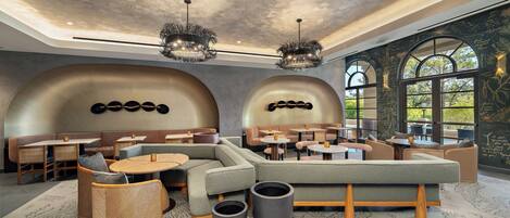 Ein moderner Lounge-Bereich mit Sitzgelegenheiten, darunter Sofas und Tische, sowie ein großes Fenster mit Blick ins Freie.