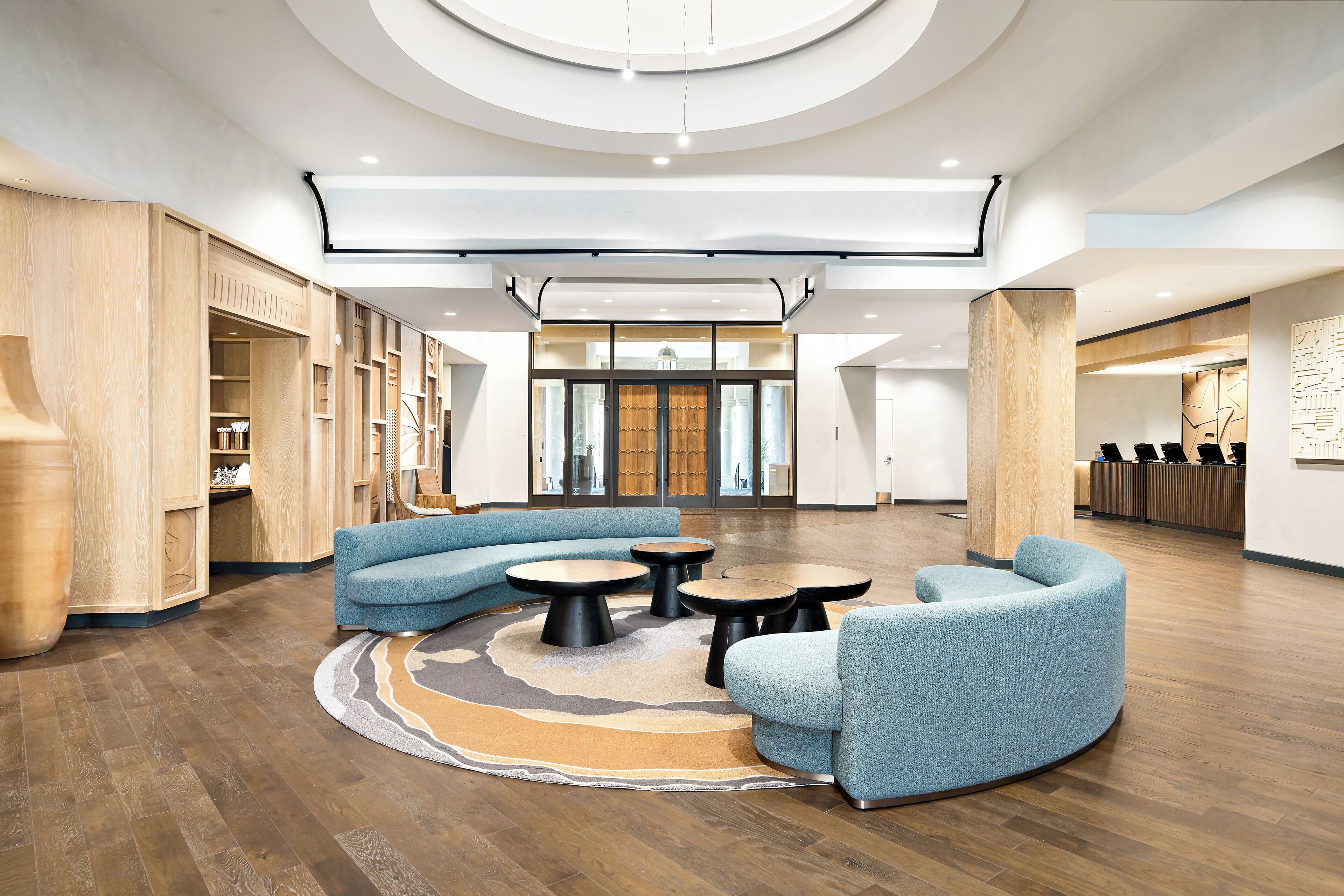 A spacious lobby with a curved blue sofa, round tables, and wooden flooring.