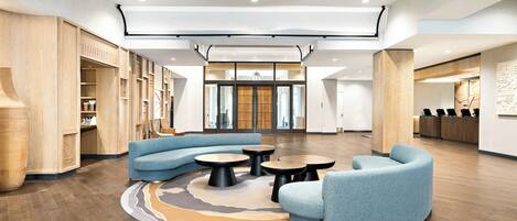 A spacious lobby with a curved blue sofa, round tables, and wooden flooring.