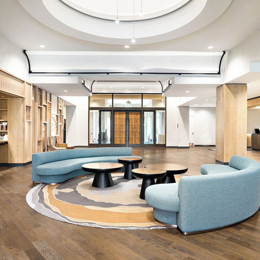A spacious lobby with a curved blue sofa, round tables, and wooden flooring.