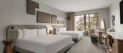Habitación de hotel con dos camas, un escritorio, una silla, una lámpara y vistas al exterior.