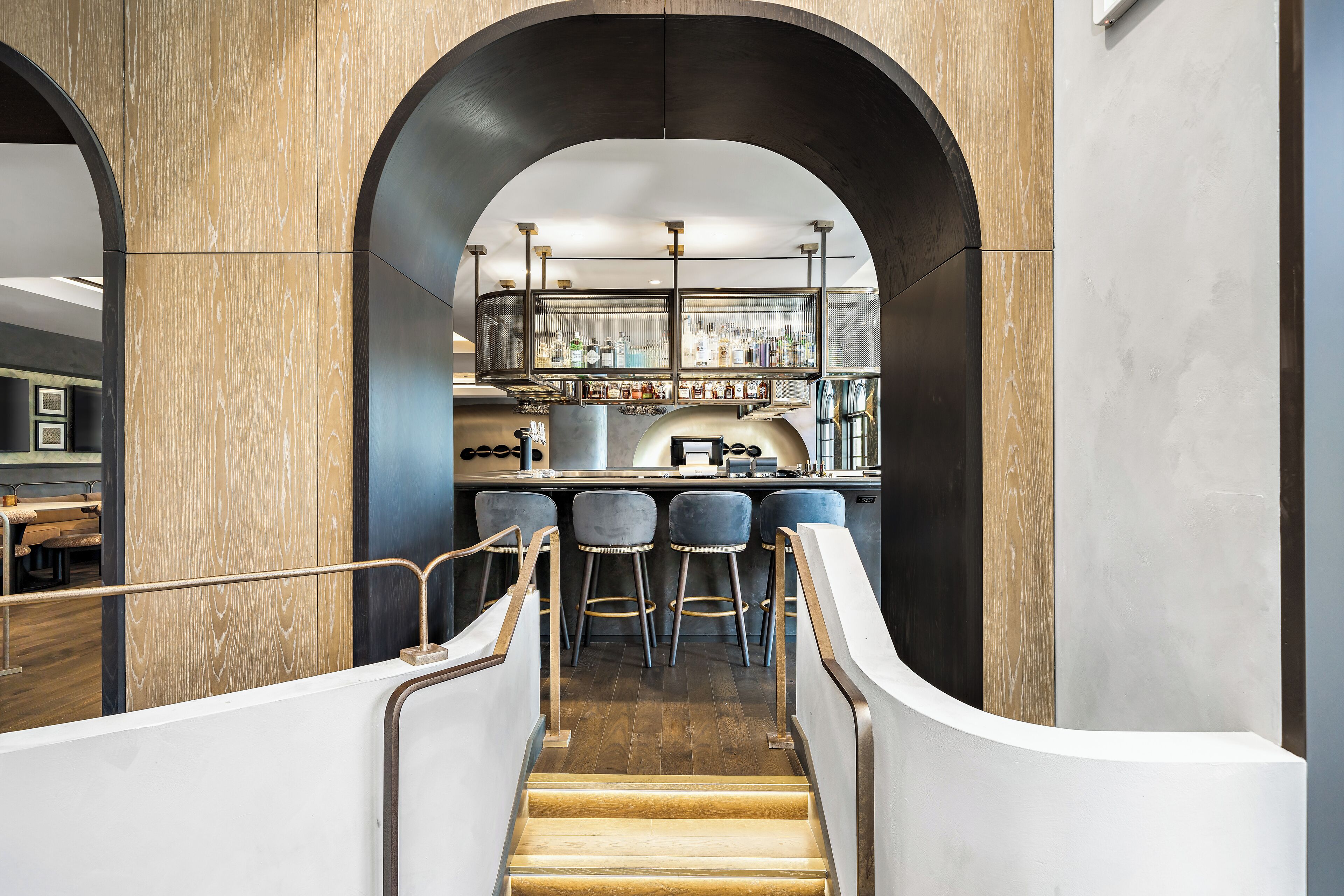 Uma área de bar moderna, com uma escadaria de madeira que leva a um espaço de estar com banquetas.