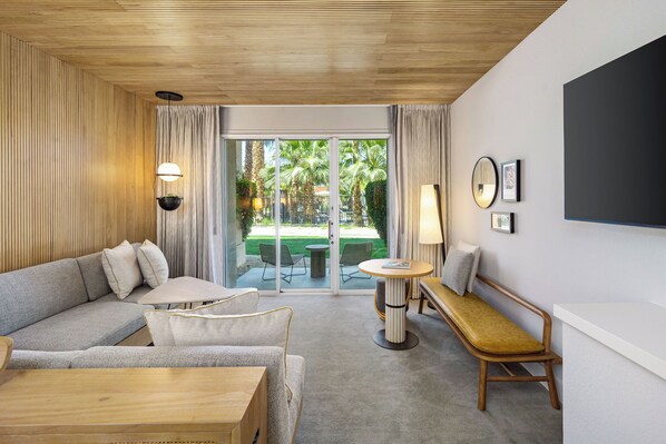 A modern hotel room with a sofa, a wooden bench, a small table, and a view of the outdoor area through a glass door. - Grand Hyatt Indian Wells Resort & Villas (Indian Wells)