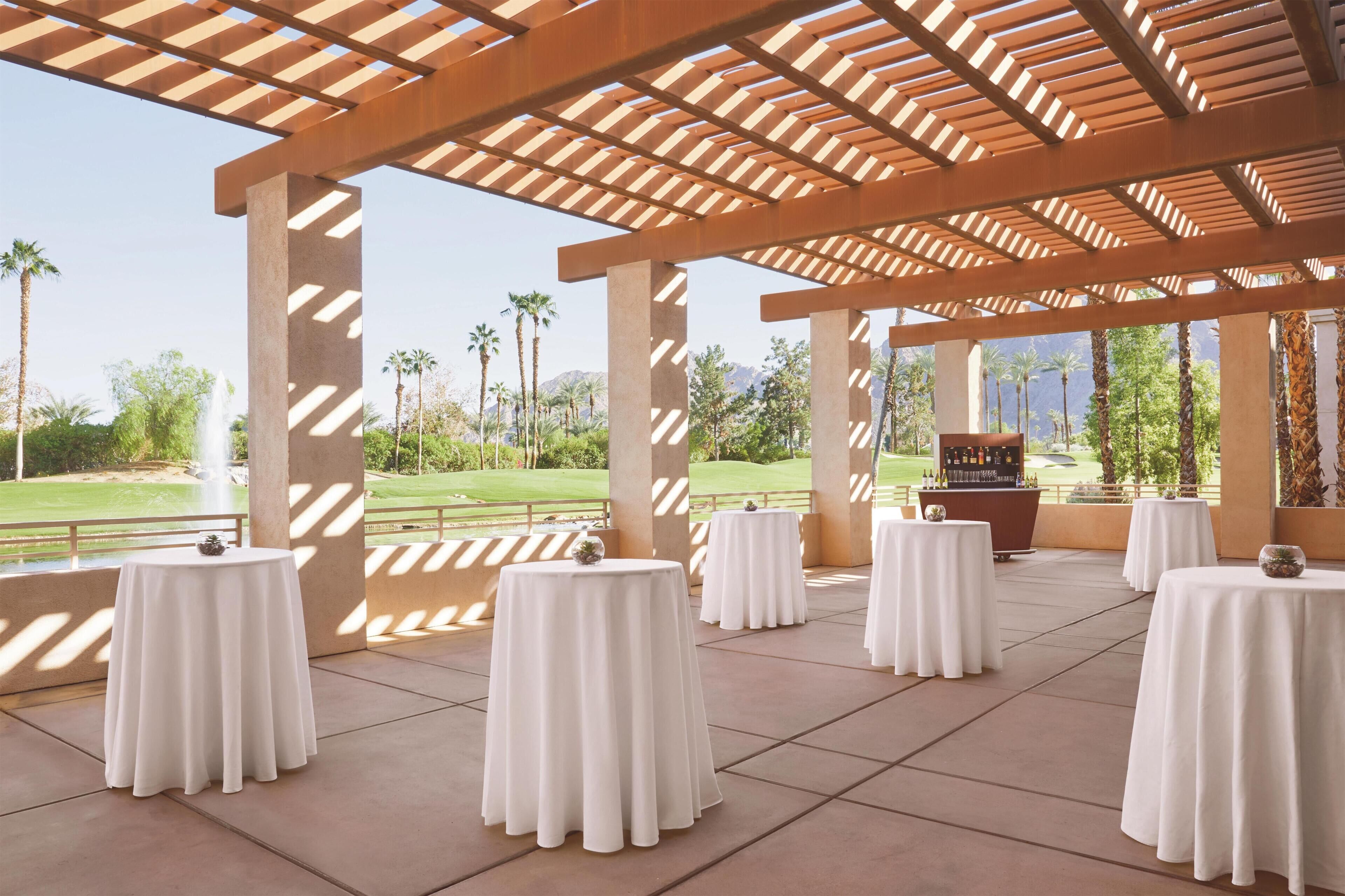 Un espacio al aire libre techado con mesas dispuestas para comer, un bar y vistas a un campo de golf.
