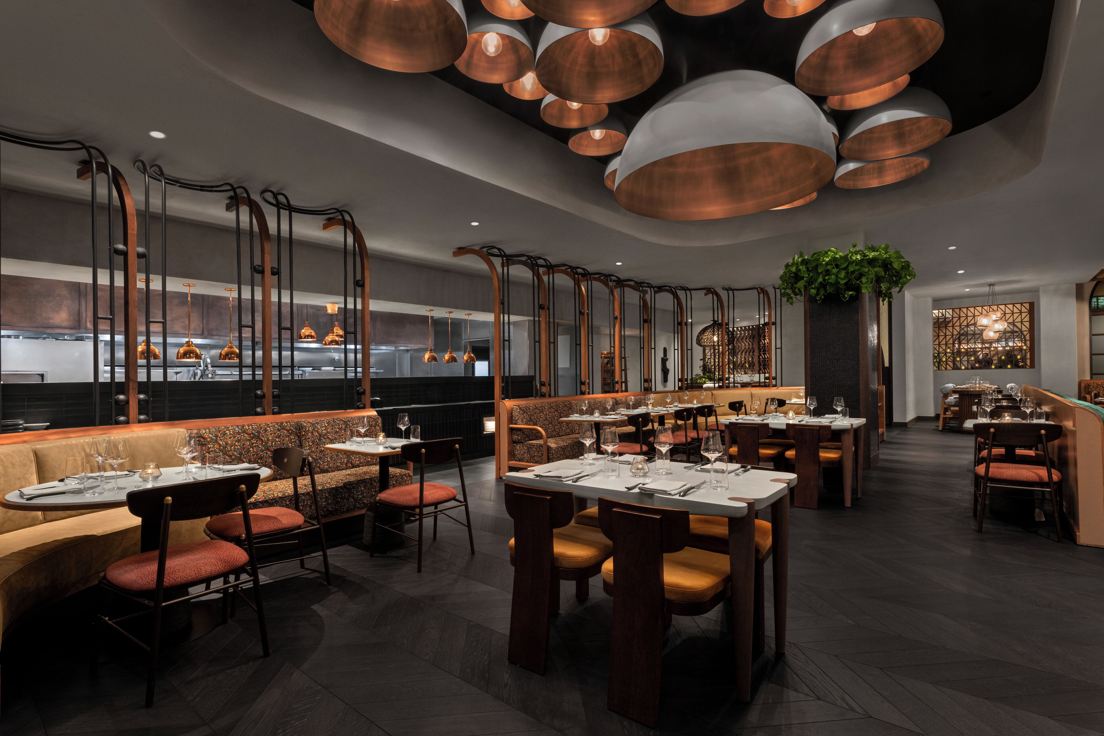 A modern restaurant interior with high ceilings, copper pendant lighting, and a mix of booth and table seating.