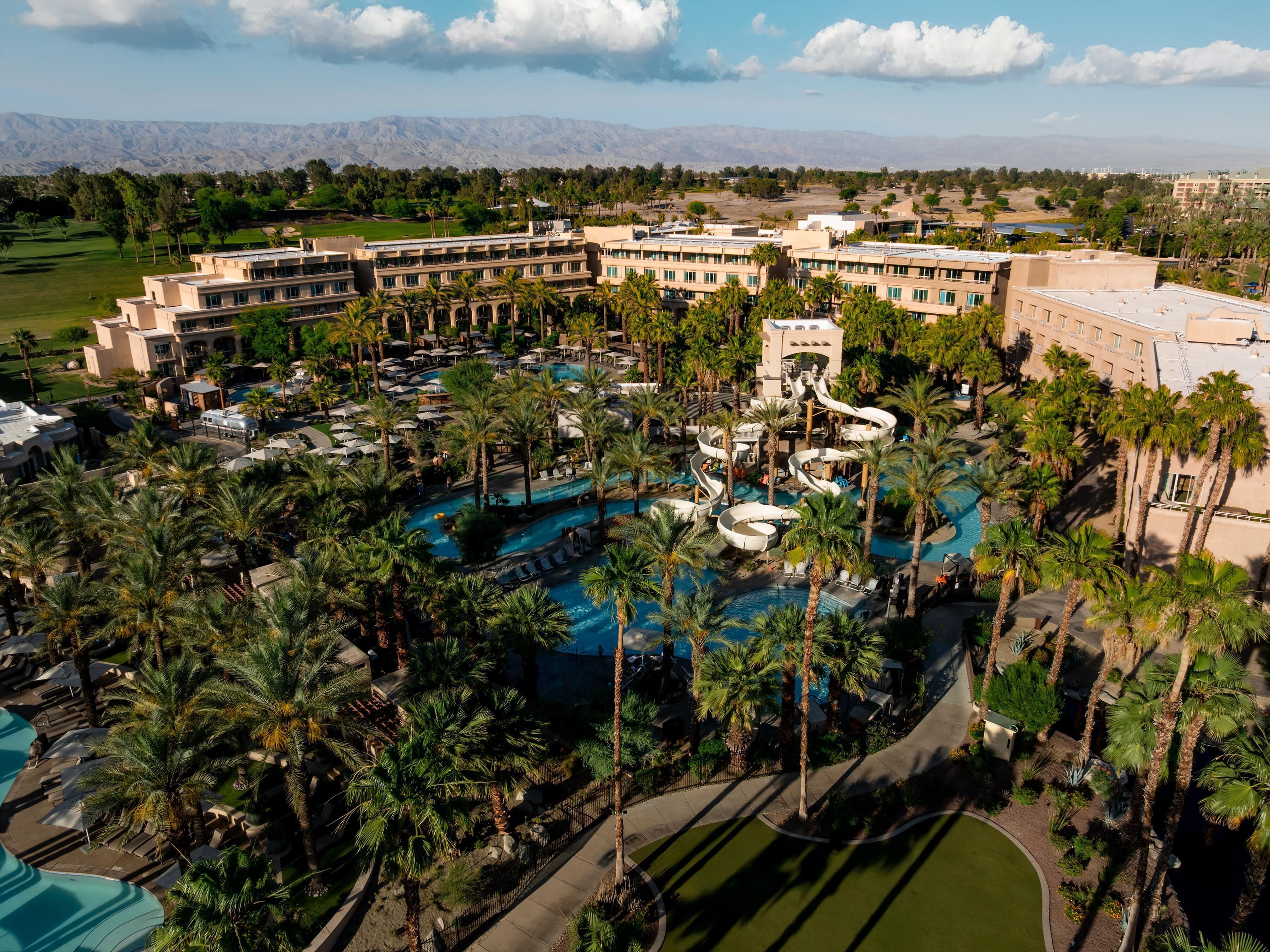A resort with multiple swimming pools, palm trees, and a mountainous backdrop.
