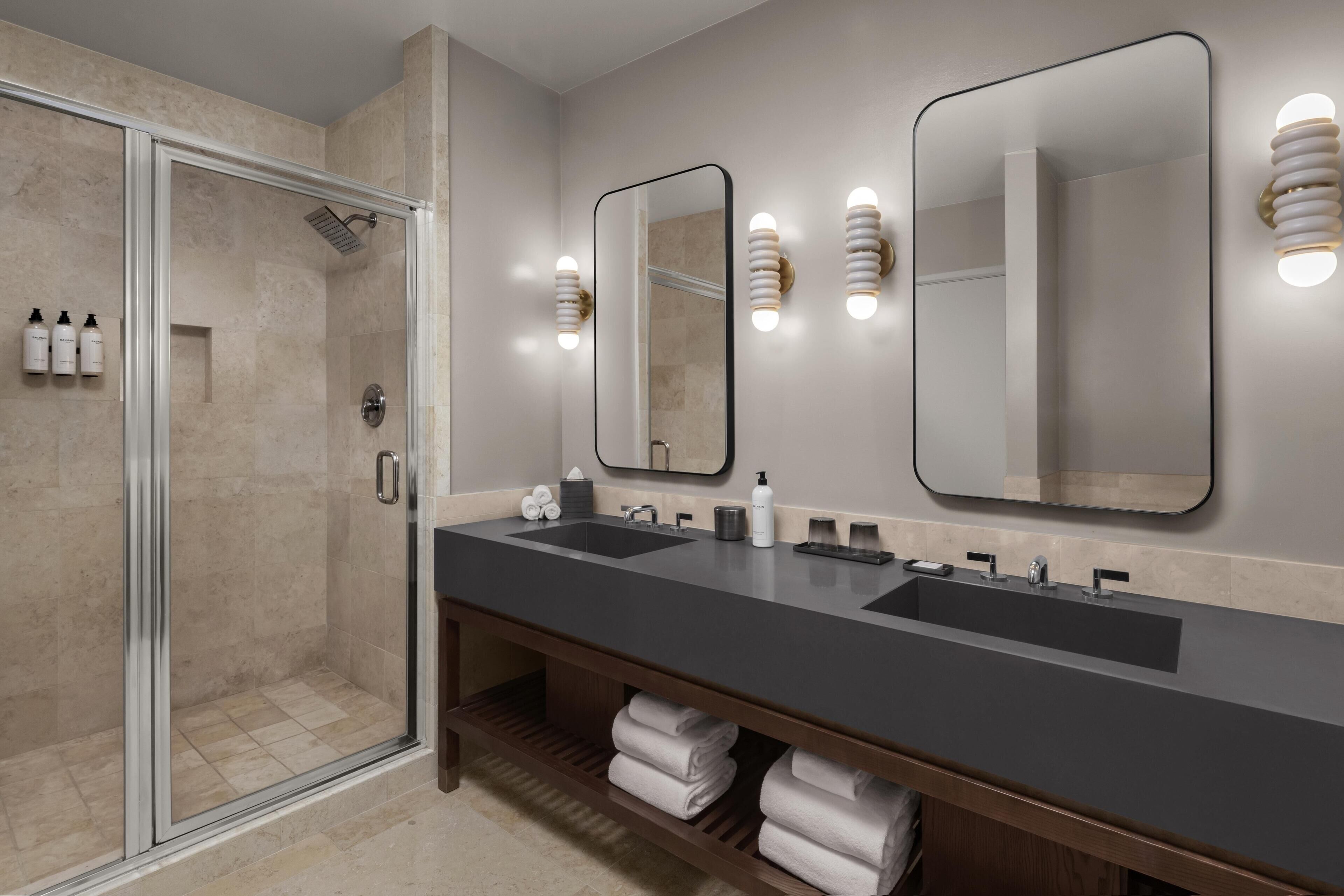 A modern bathroom with a glass-enclosed shower, two sinks, and wall-mounted mirrors.