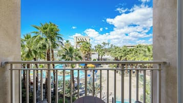 A balcony with a view of a pool area, palm trees, and a building in the background.