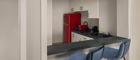Una cocina con armarios blancos, un refrigerador rojo, una encimera negra y dos taburetes azules.