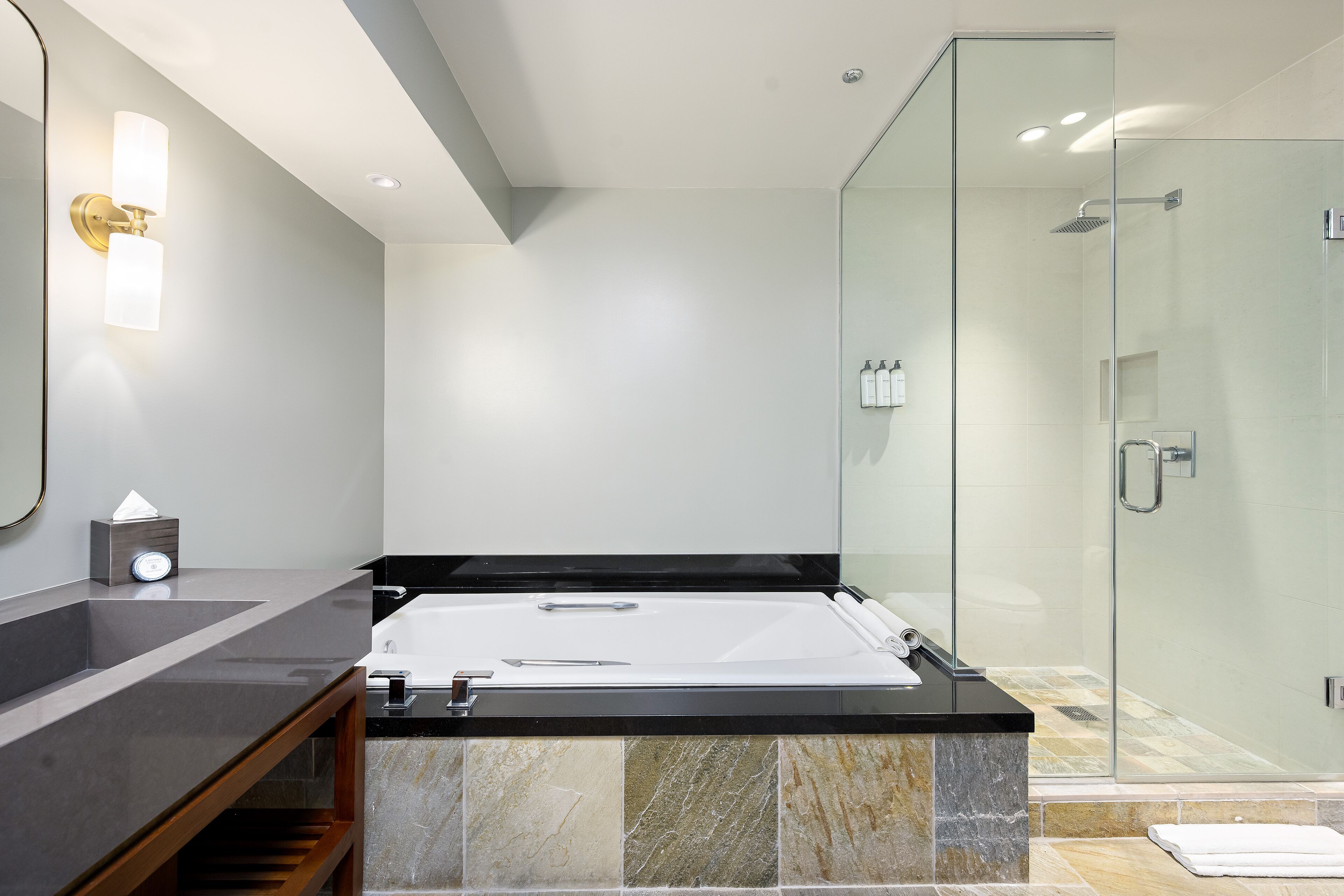Un baño moderno con una bañera grande, ducha con cerramiento de vidrio y tocador con espejo e iluminación.
