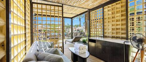 Un área de estar al aire libre con luz solar, techo de madera, bar junto a la piscina y vistas a la piscina y palmeras.