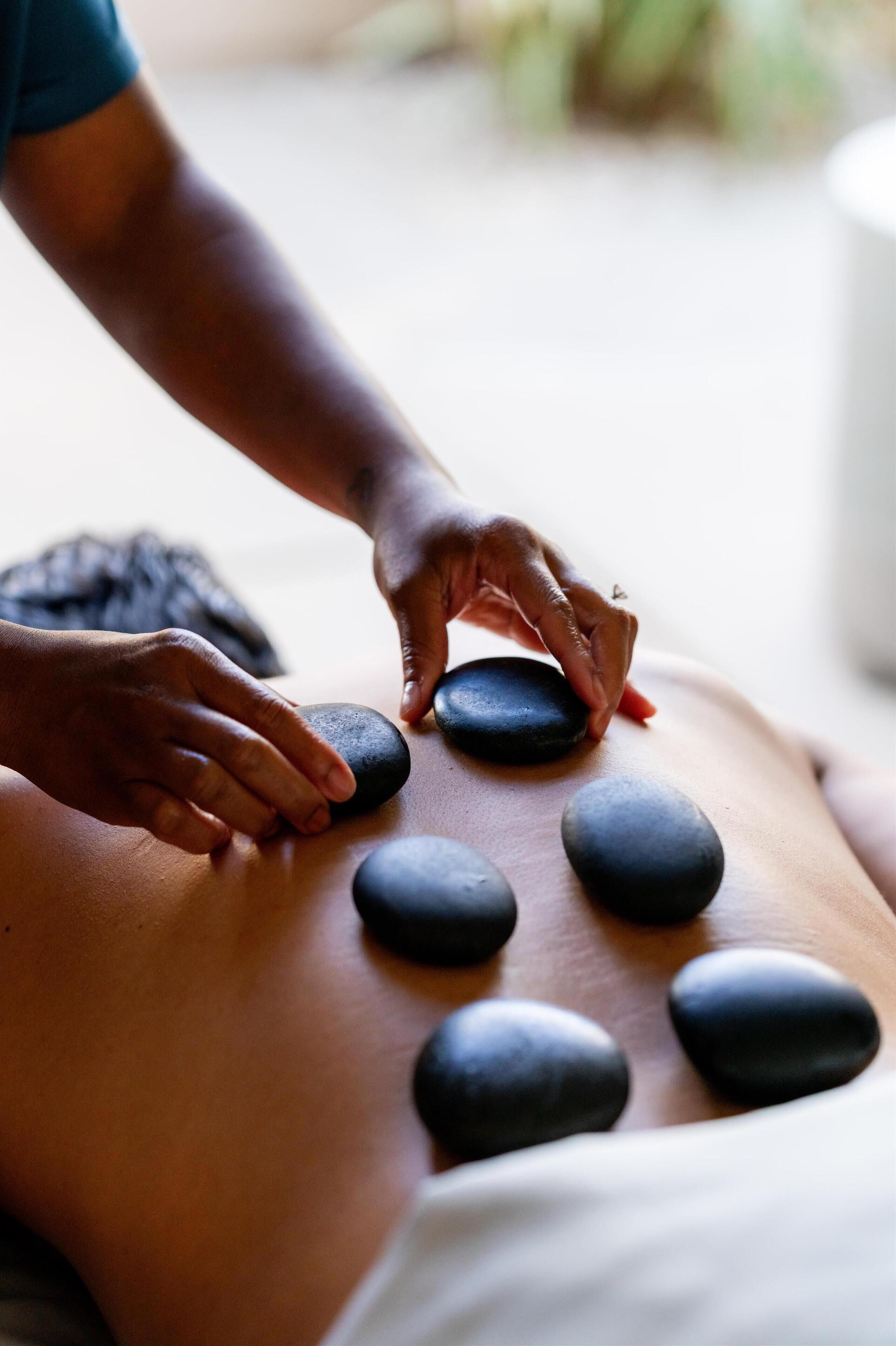 A person receiving a stone massage with multiple black stones placed on their back.