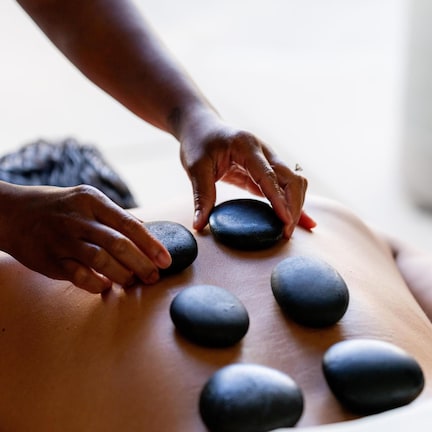 A person receiving a stone massage with multiple black stones placed on their back.