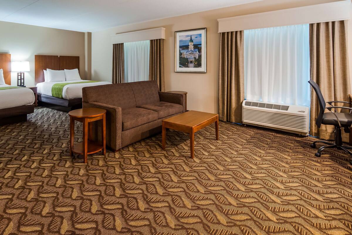 A hotel room with a bed, a sofa, a small table, a chair, and a large window with curtains.