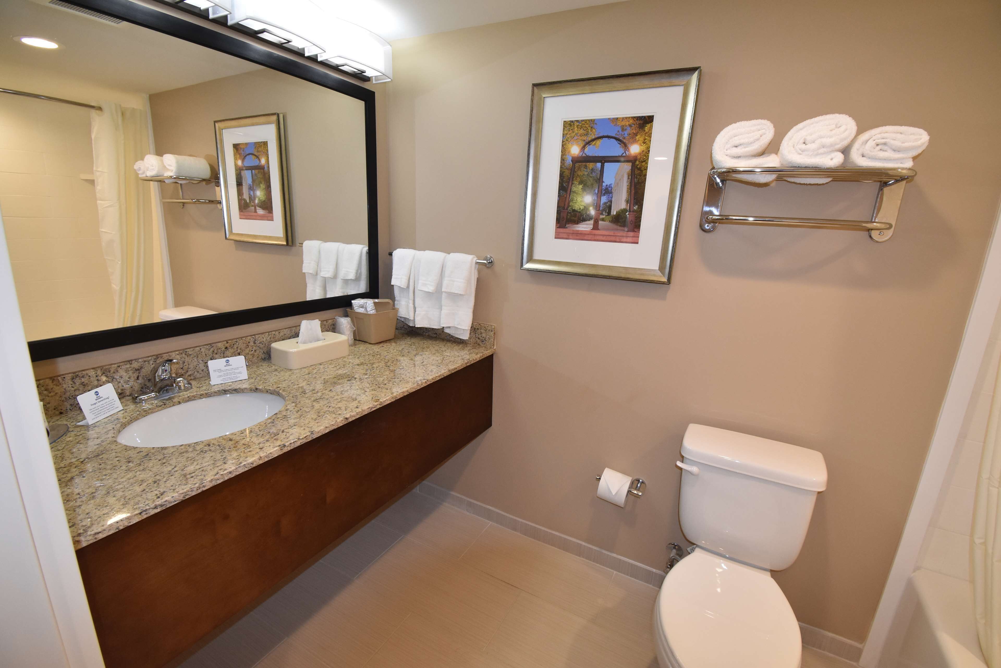 A bathroom with two sinks, a toilet, a towel rack, and framed pictures on the wall.