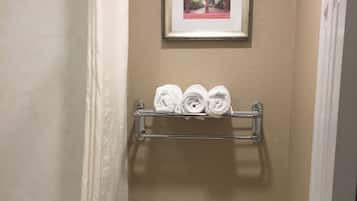 A bathroom with a toilet, a shower curtain, a towel rack with towels, and a framed picture on the wall.
