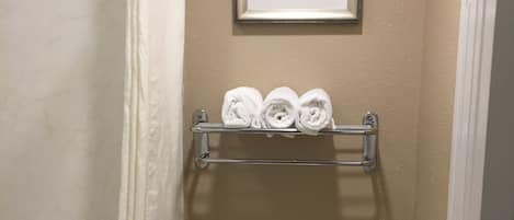 A bathroom with a toilet, a shower curtain, a towel rack with towels, and a framed picture on the wall.