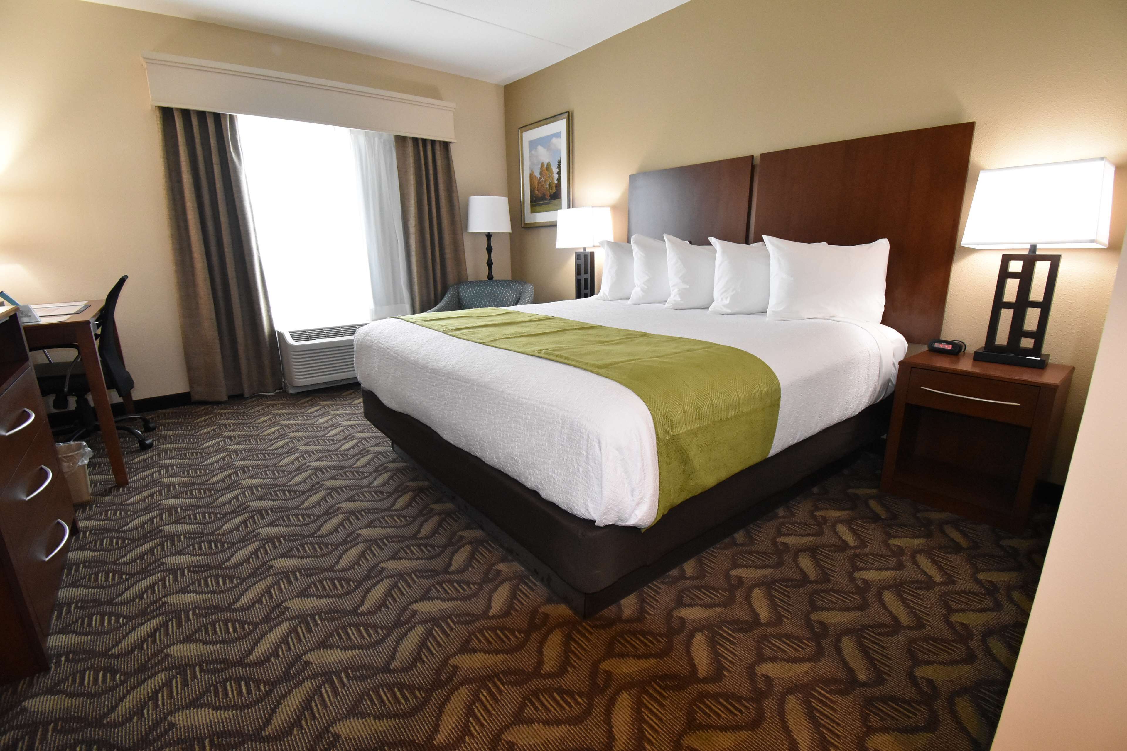 Una habitación de hotel con una cama grande, un escritorio, una silla, una lámpara y un cuadro en la pared.
