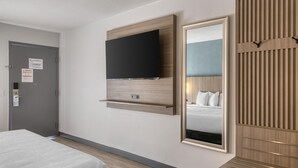 Une chambre d’hôtel avec un lit, un téléviseur fixé au mur, un miroir et un mur recouvert de panneaux en bois.