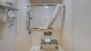 Zona de ducha con barra de apoyo, asiento para ducha y toallero.