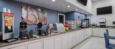 Zona de desayuno autoservicio con máquinas de café, microondas y dispensador de bebidas.