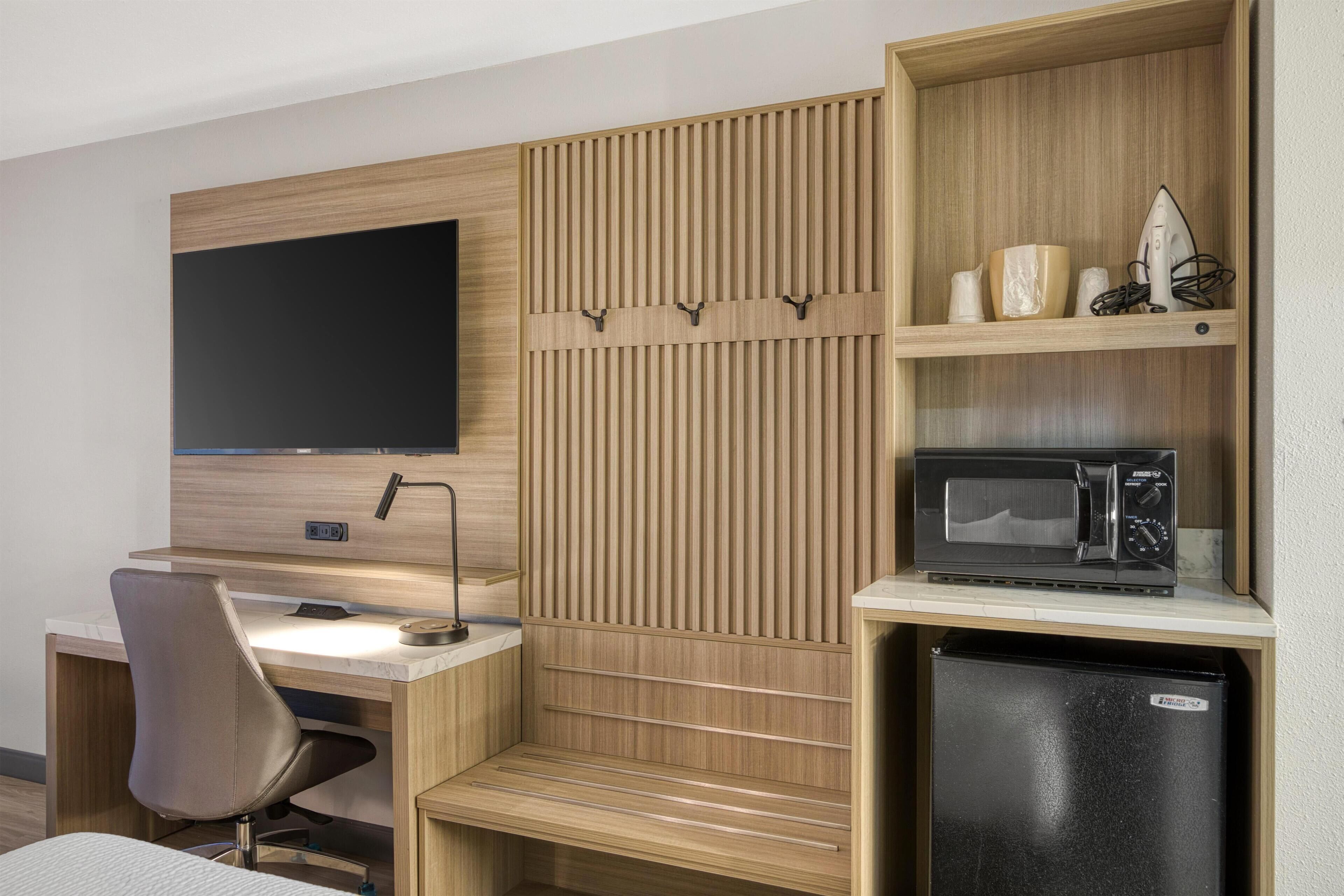 Habitación de hotel pequeña con escritorio de madera, una silla, televisor de pantalla plana, microondas y refrigerador.