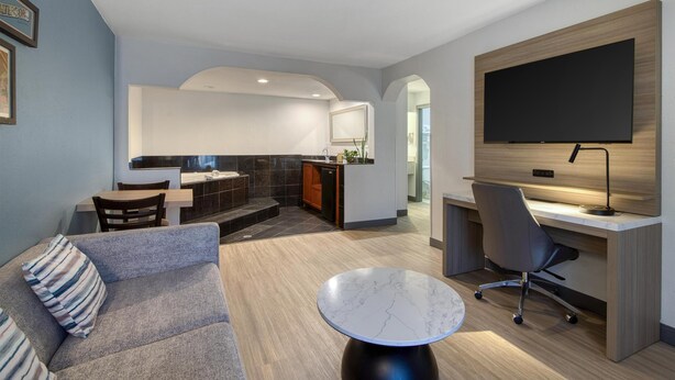 Un salon moderne avec un canapé, une table ronde, un téléviseur fixé à un mur en bois, et un coin cuisine à l’arrière-plan.