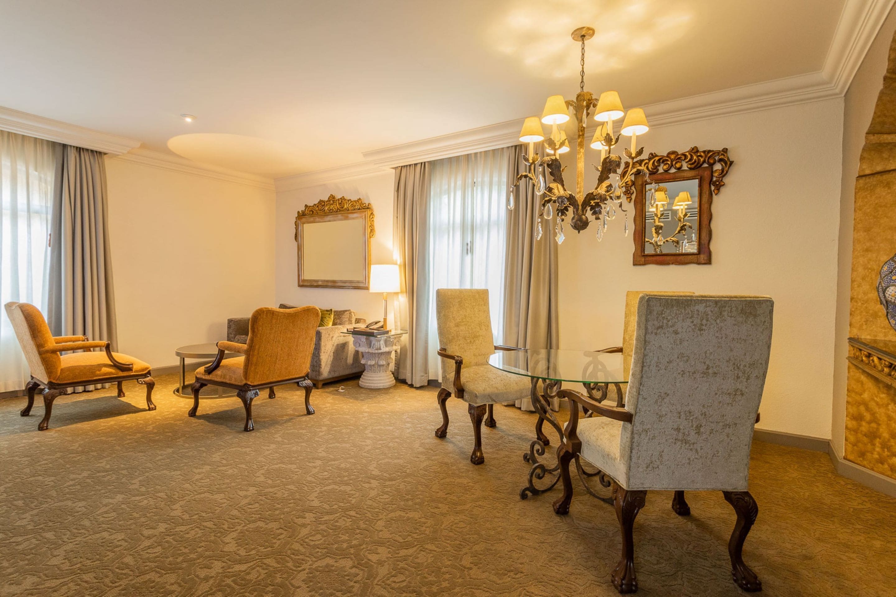 A hotel room with a dining area featuring a chandelier, a round table, and four chairs.