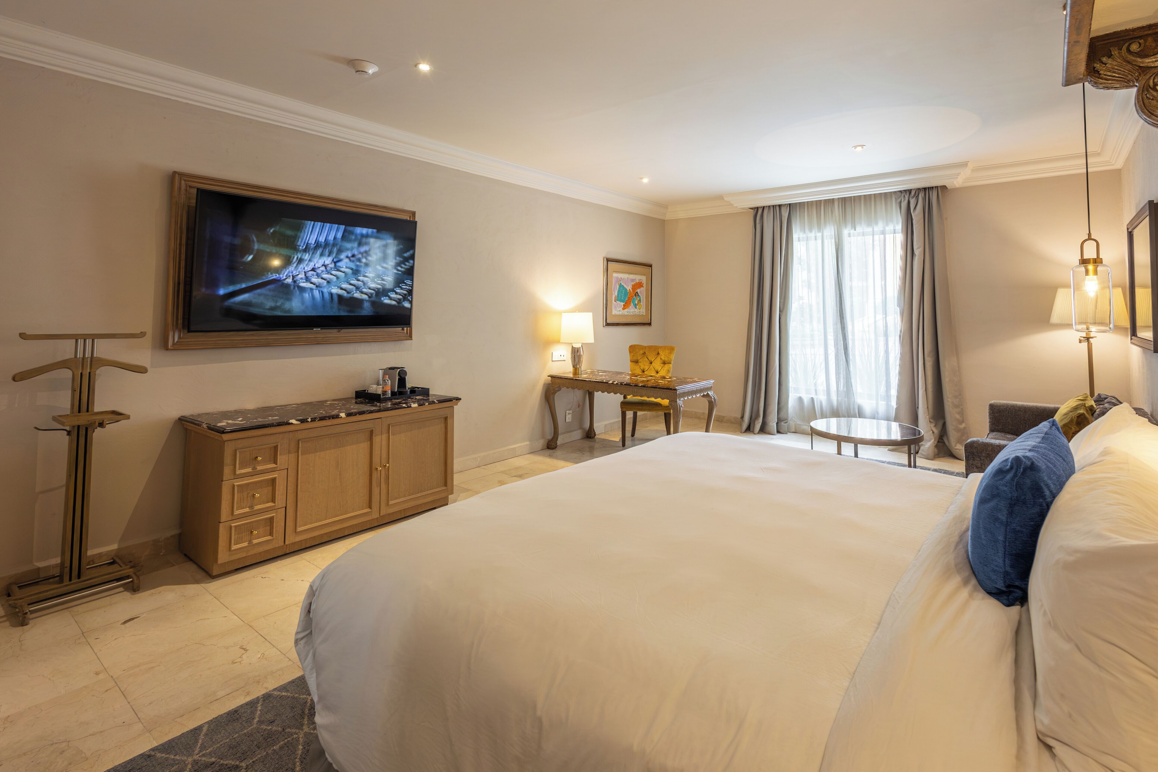 A hotel room with a large bed, a desk, a chair, a television, and a window with curtains.