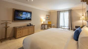 A hotel room with a large bed, a desk, a chair, a television, and a window with curtains.